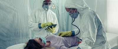 two healthcare workers tending to a patient in isolation on a gurney two healthcare workers tending to a patient in isolation on a gurney